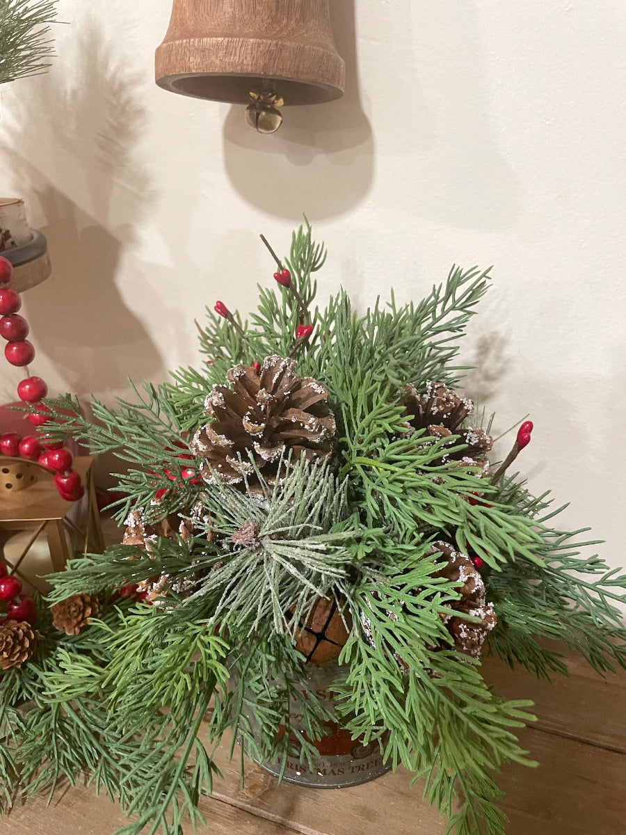 faux evergreen arrangement in metal vase with red truck on it, with pinecones and metal bells