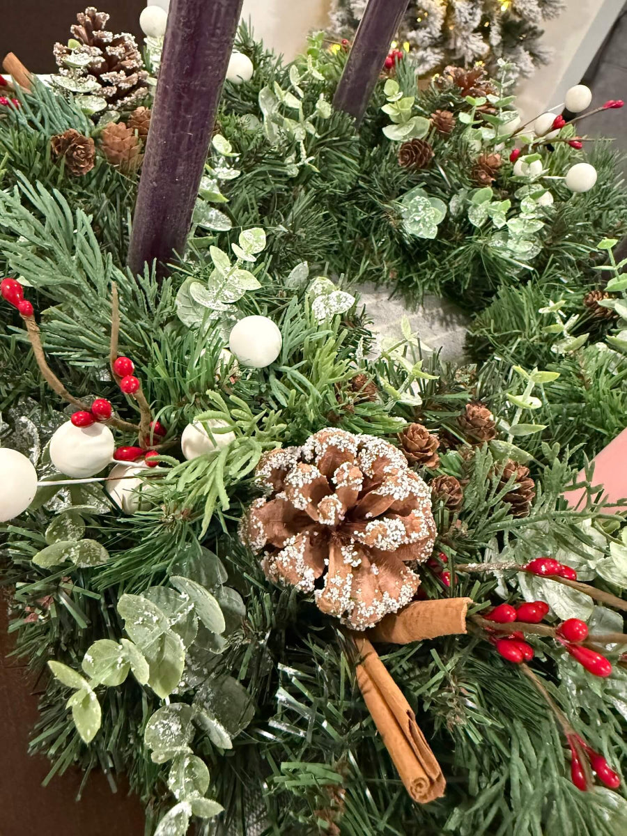 close up for handmade lush elegant evergreen advent wreath with arborvitae and snowy eucalyptus stems decorated with pinecones, red and white berries and cinnamon stick, with four taper candles in purple/pink, red or white perfect for dining table