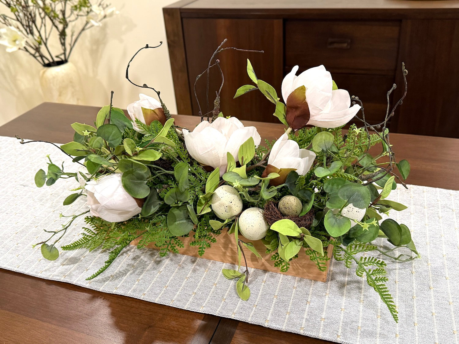 white magnolia flowers, fake greenery, faux eggs and nest in long wooden planter