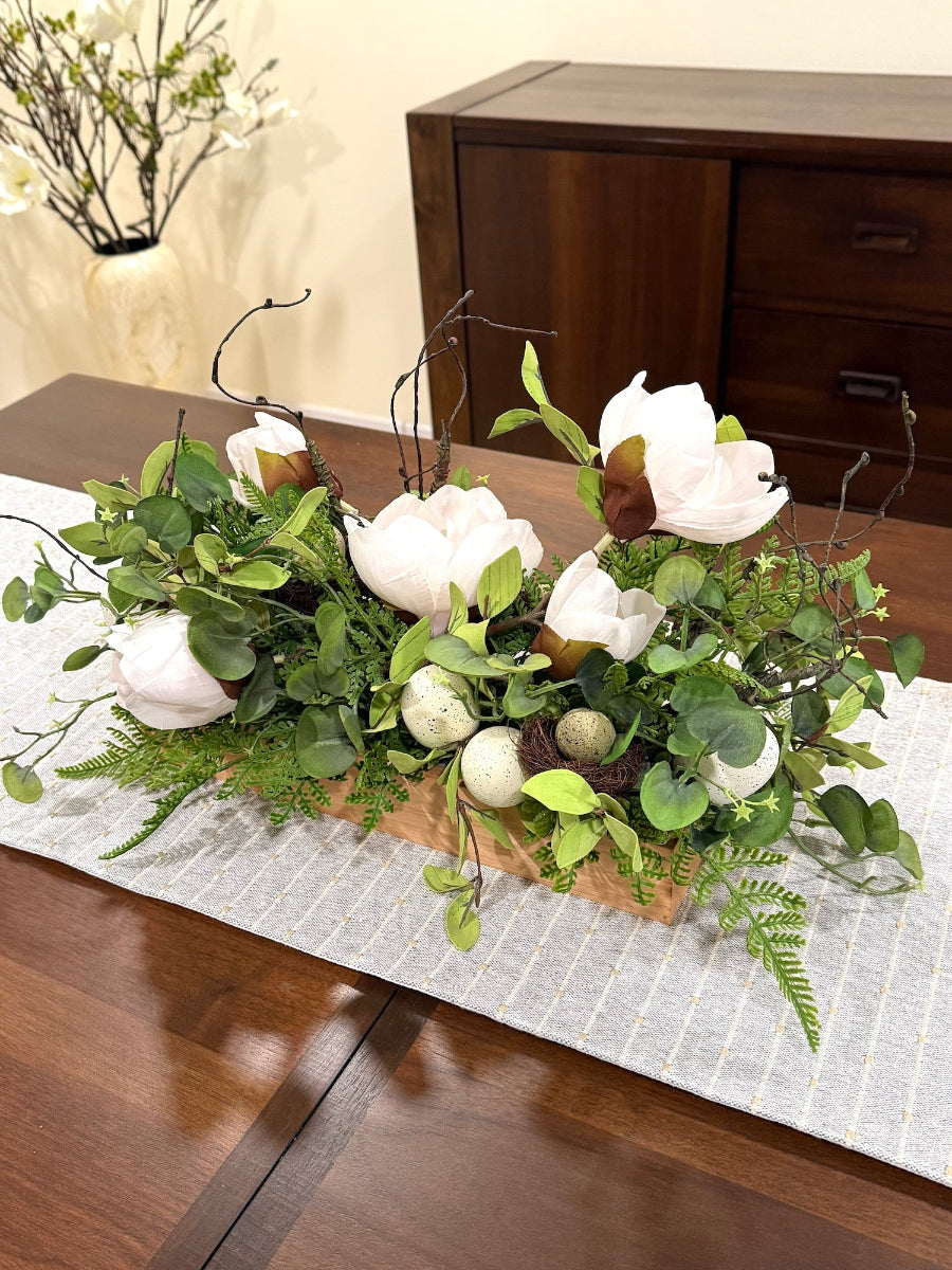 easter arrangement with artificial greenery fake white magnolia flowers and faux eggs  and faux nest in wooden planter