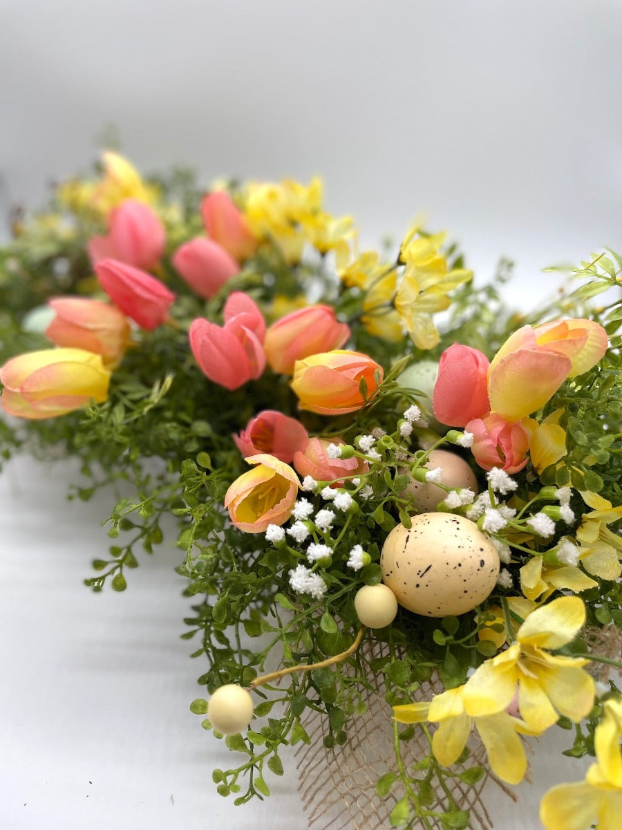 Easter Centerpiece with pink and yello tulips, variety of greenery, delicate white flowers, faux eggs in whitewashed wooden planter decorated with burlap