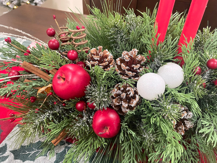 Decorative Christmas arrangement with variety of greenery, red berries, apples, pinecones, and white ornaments