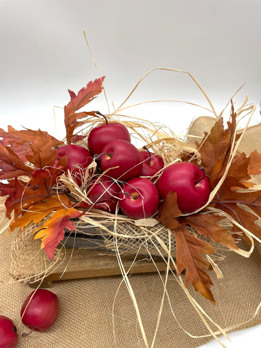 Decorative arrangement with red apples, brown leaves, and straw in wooden crate