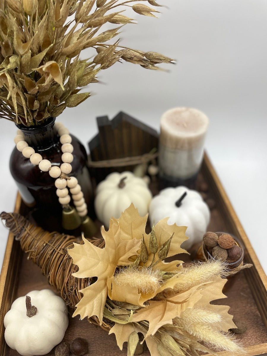 Fall Tray Decor with wheat arrangement in brown lass bottle vase, jar with faux acorns, white faux pumpkins, candle, wooden home sign on square wooden tray