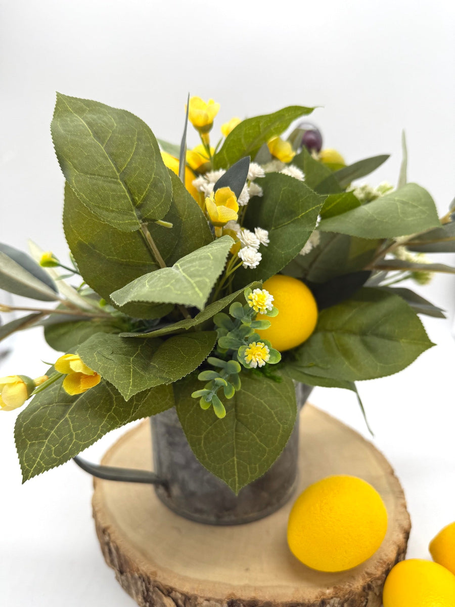 artificial greenery, faux lemons, white and yellow flowers in metal watering can
