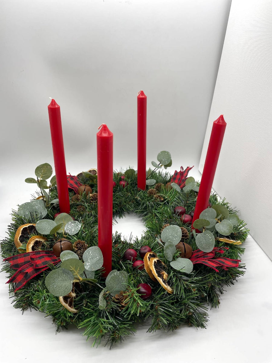 christmas advent wreath with natural elements of cranberries, dried lemon slices, pinecones, metal bells and red-black ribbon for rustic look with red tapper candles
