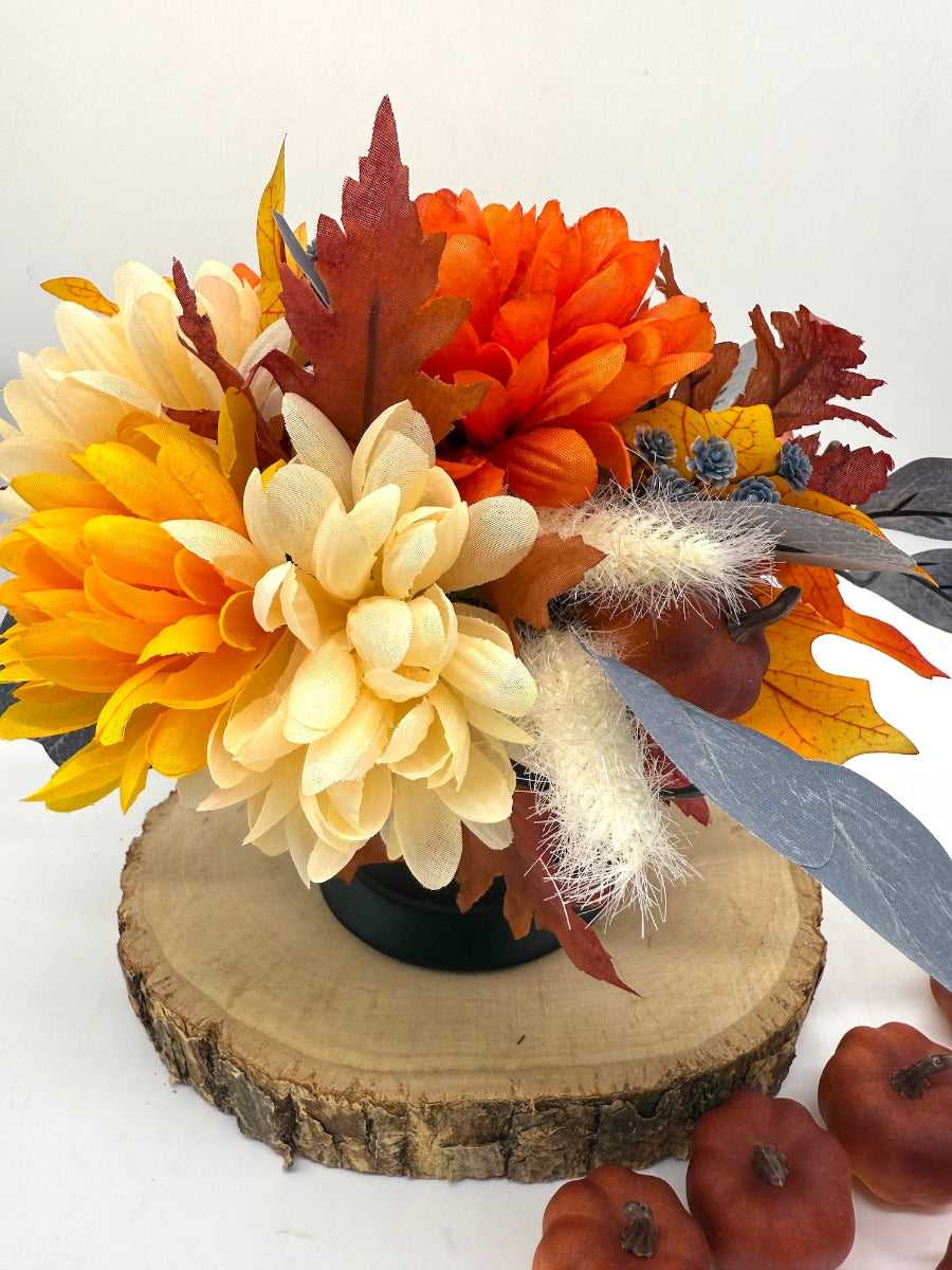 Autumn-themed orange-yellow-blue floral arrangement with blue pumpkin in black ceramic vase