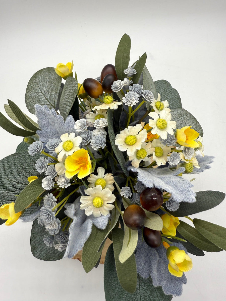 mix of yellow and blue flowers with silver ucalyptus and olive stems in small ceramic vase