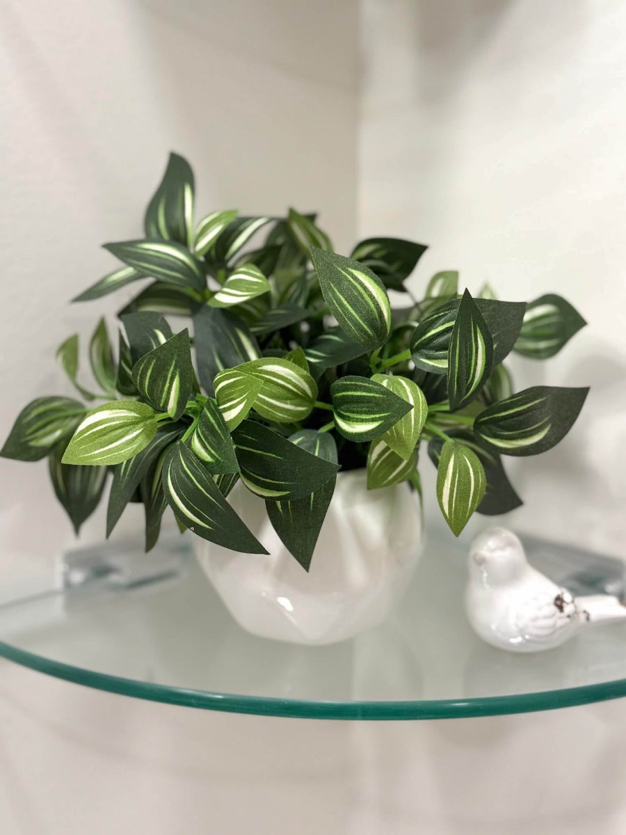 small faux plant with green leaves and white stripes in white cearic pot of geometric shape on bathroom shelf