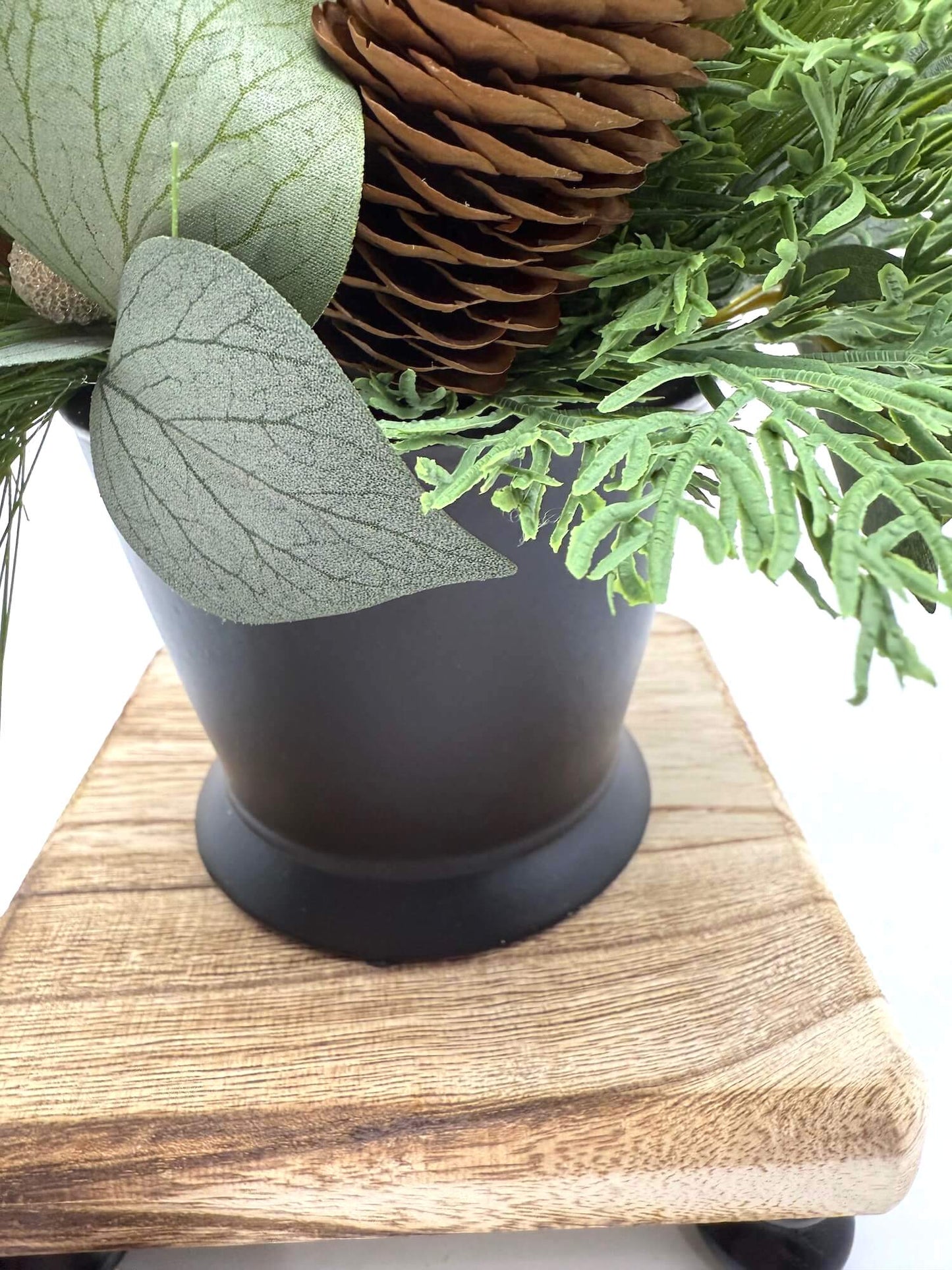 black ceramic pot for small winter arrangements with evergreen stems and pinecones, cinnamon sticks and berries in neutral tones