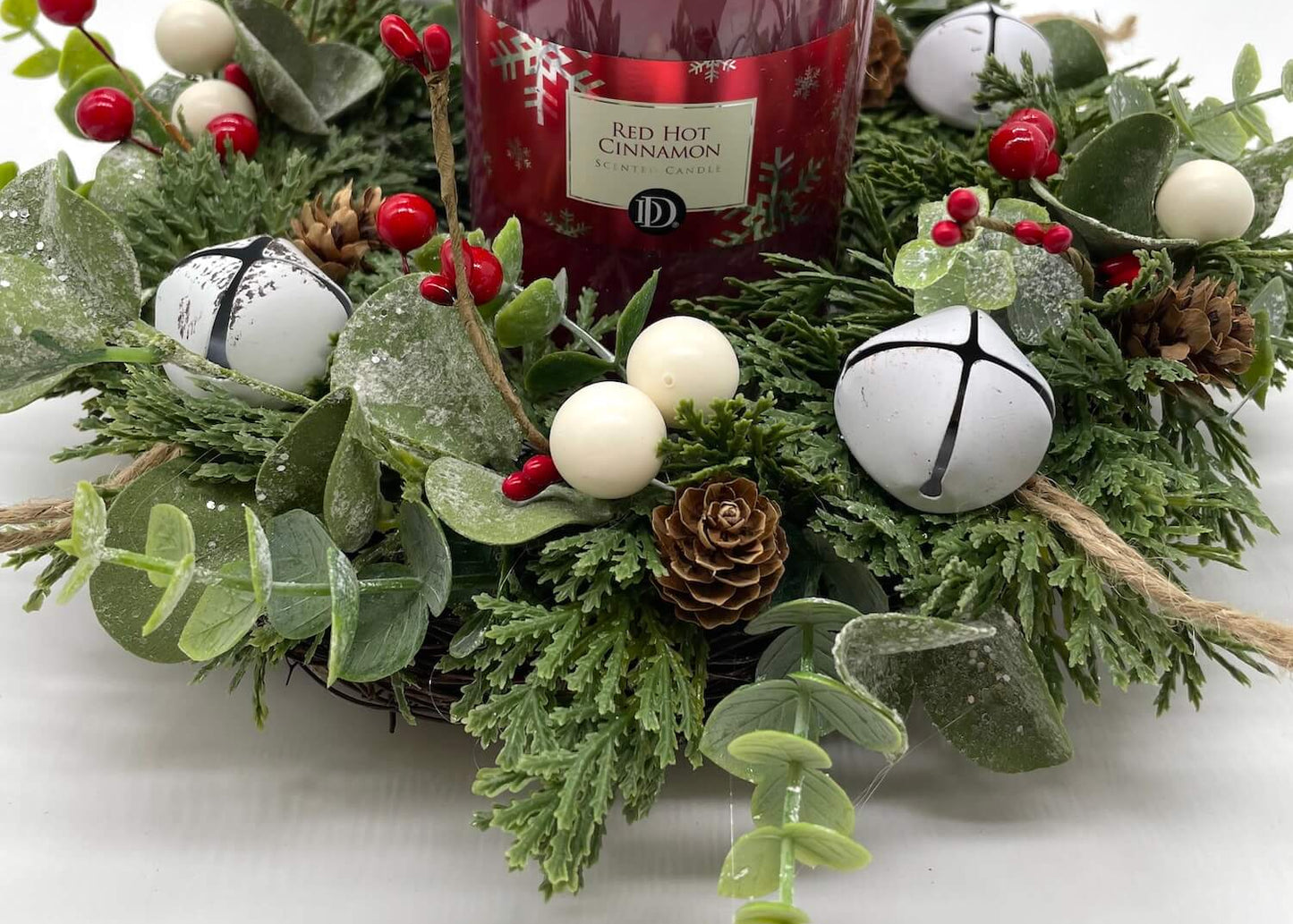 winter evergreen table wreath with greenery, red and white berries, white bells, and red pillar candle in the middle
