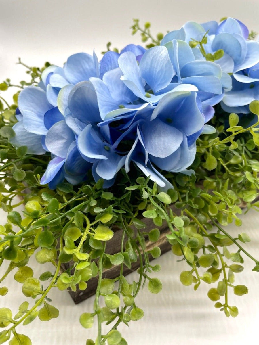 close up of blue hydrangea with realistic greenery in wooden planter in expresso color
