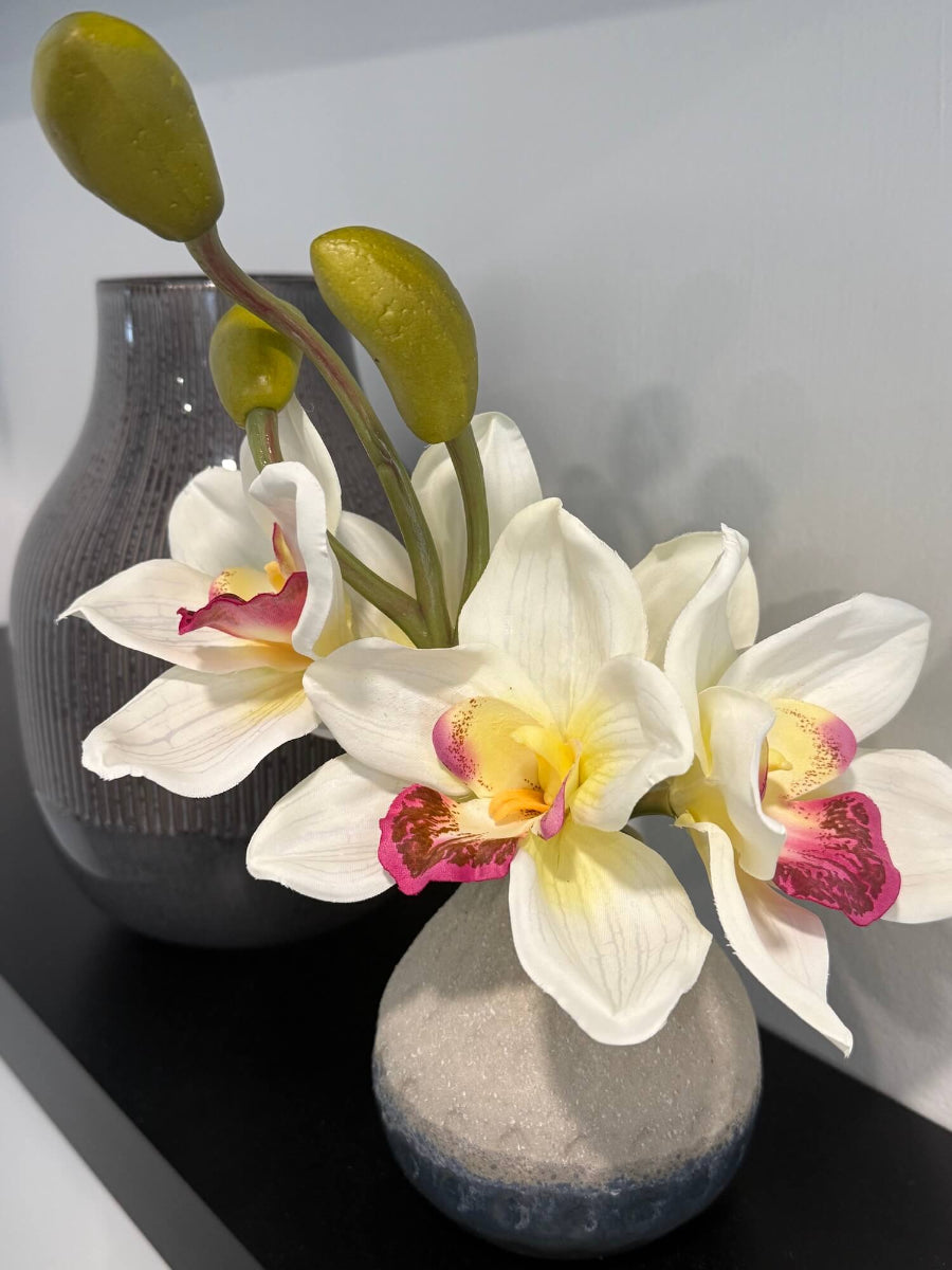 realistic looking small white orchid arrangement of five flowers and 3 buds in gray ceramic vase styled on shelf