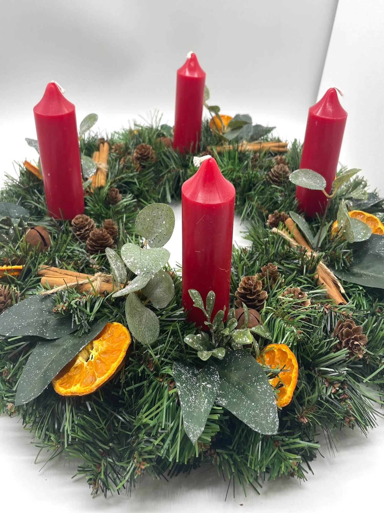 rustic advent wreath with earthy elements of cinnamon stick, dried orange slices, pinecones, winter greenery, metal bels and thick short red candles
