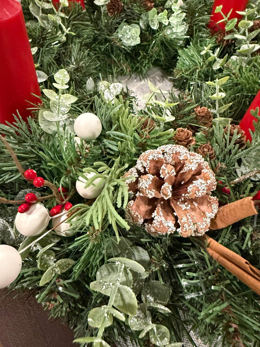 close up for lush elegant handmade advent wreath with pine, arborvitae and snowy eucalyptus stems, with snowy and plain pinecones, cinnamon sticks, red and white berries, with short thick candles or purple/pink candles set on dining table