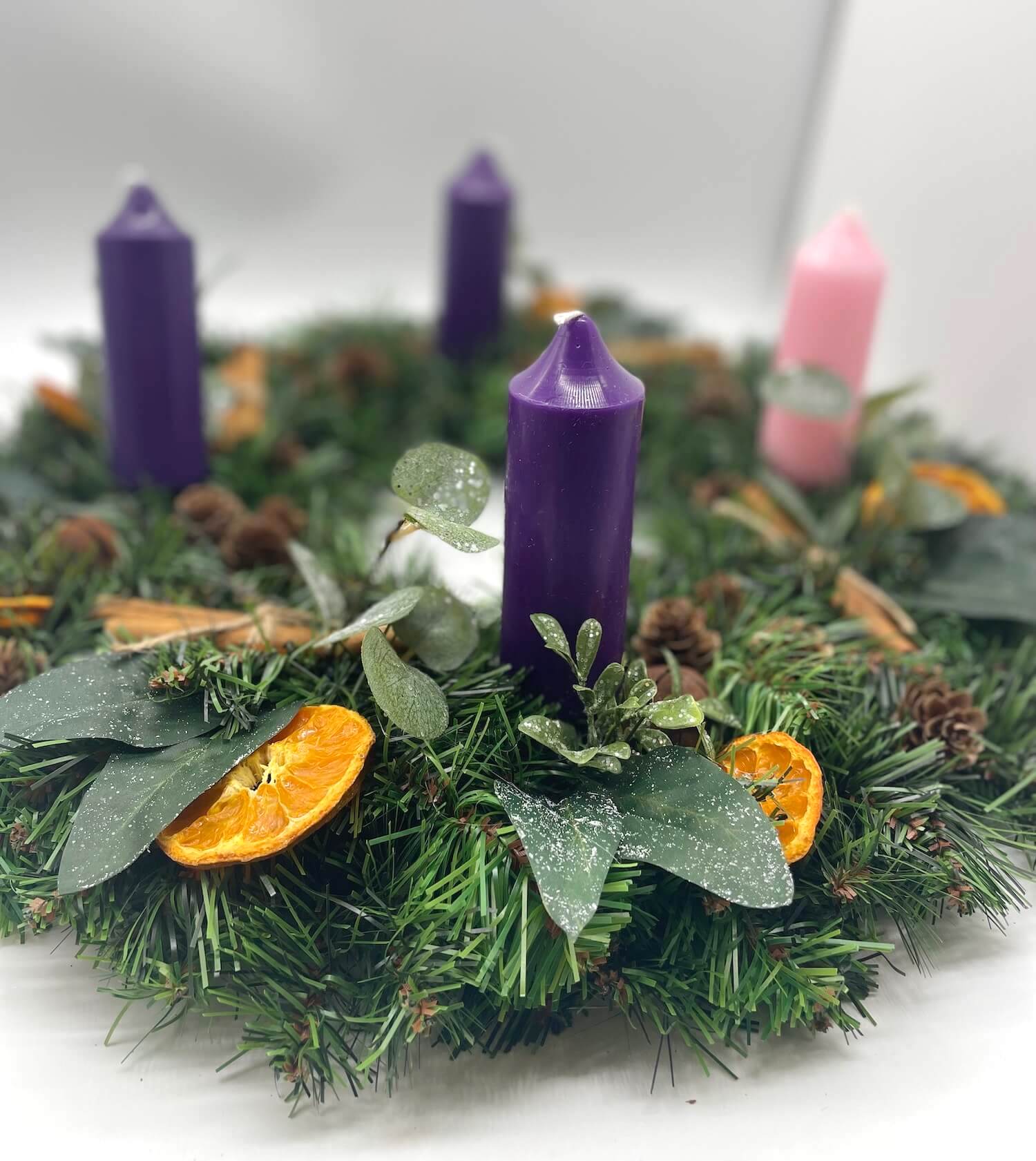 farmhouse rustic advent wreath with earthy elements of cinnamon stick, dried orange slices, pinecones, winter greenery, metal bels and thick short purple pink candles