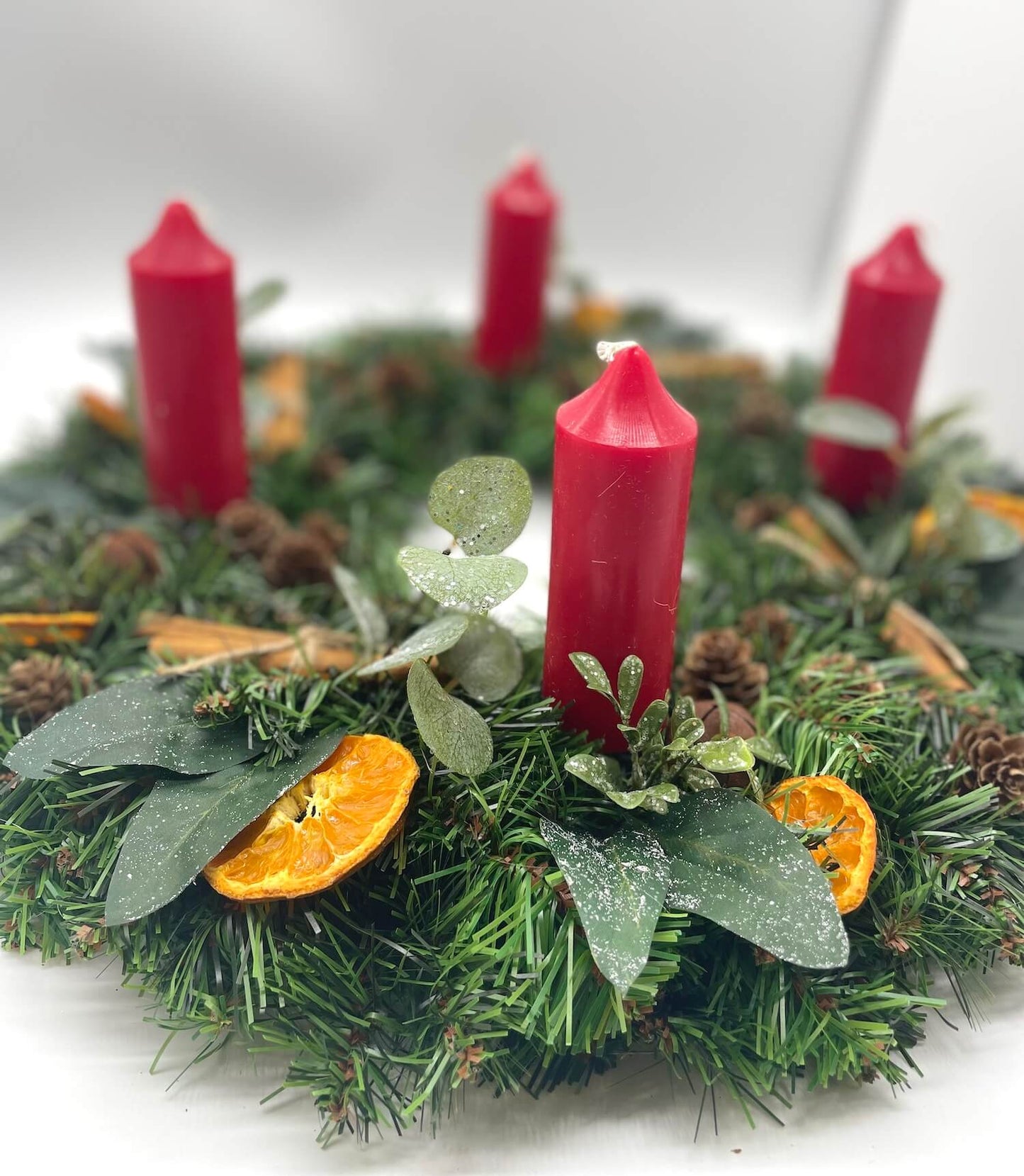 farmhouse rustic advent wreath with earthy elements of cinnamon stick, dried orange slices, pinecones, winter greenery, metal bels and thick short red candles