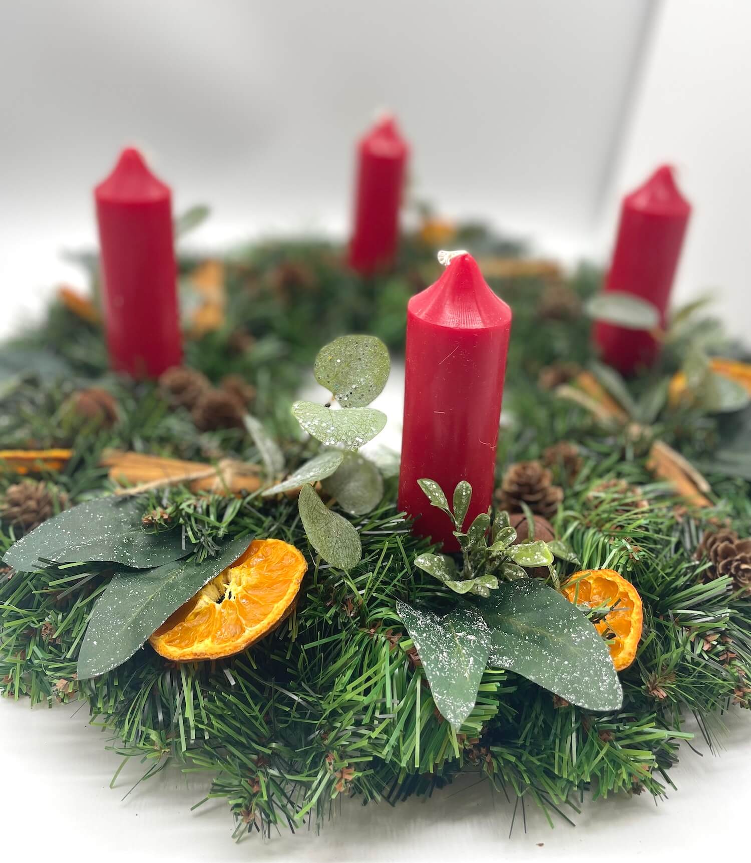 farmhouse rustic advent wreath with earthy elements of cinnamon stick, dried orange slices, pinecones, winter greenery, metal bels and thick short red candles