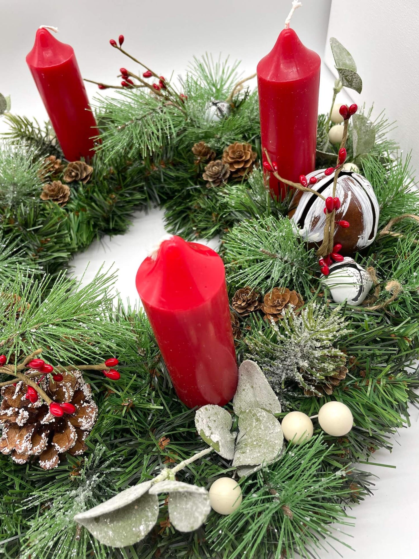 close up of handmade evergreen Advent wreath with red candles, pine cones, metal bells, greenery and berries