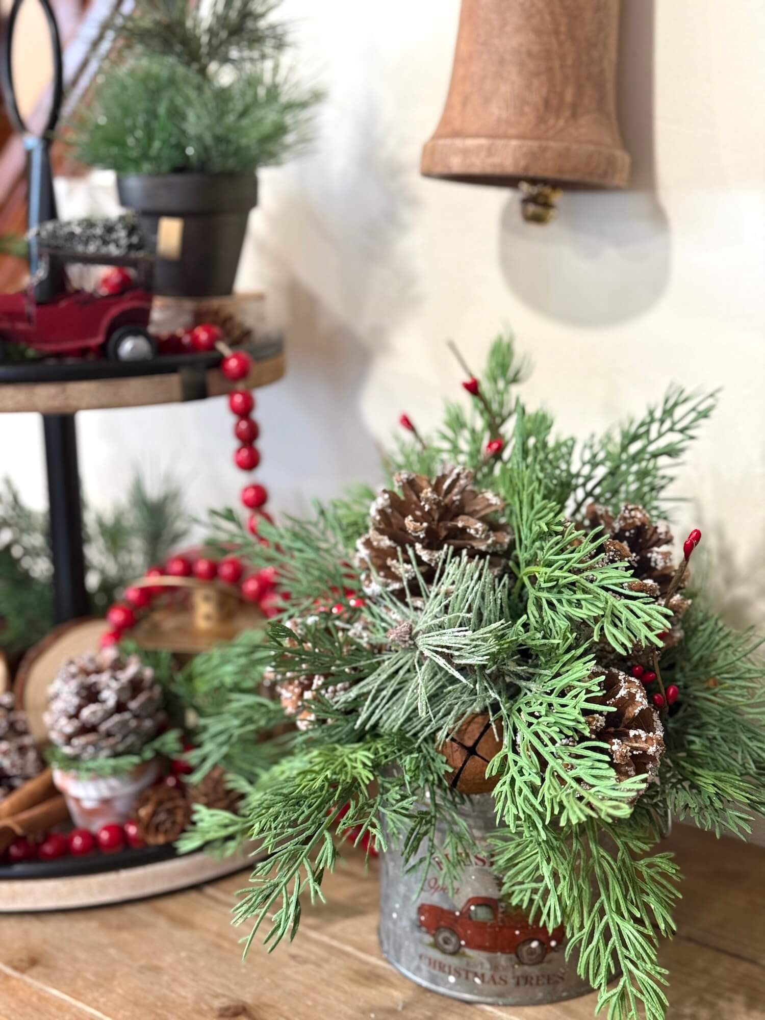 christmas evergreen arrangement with pinecones metal bell and red berries in metal can with red truck