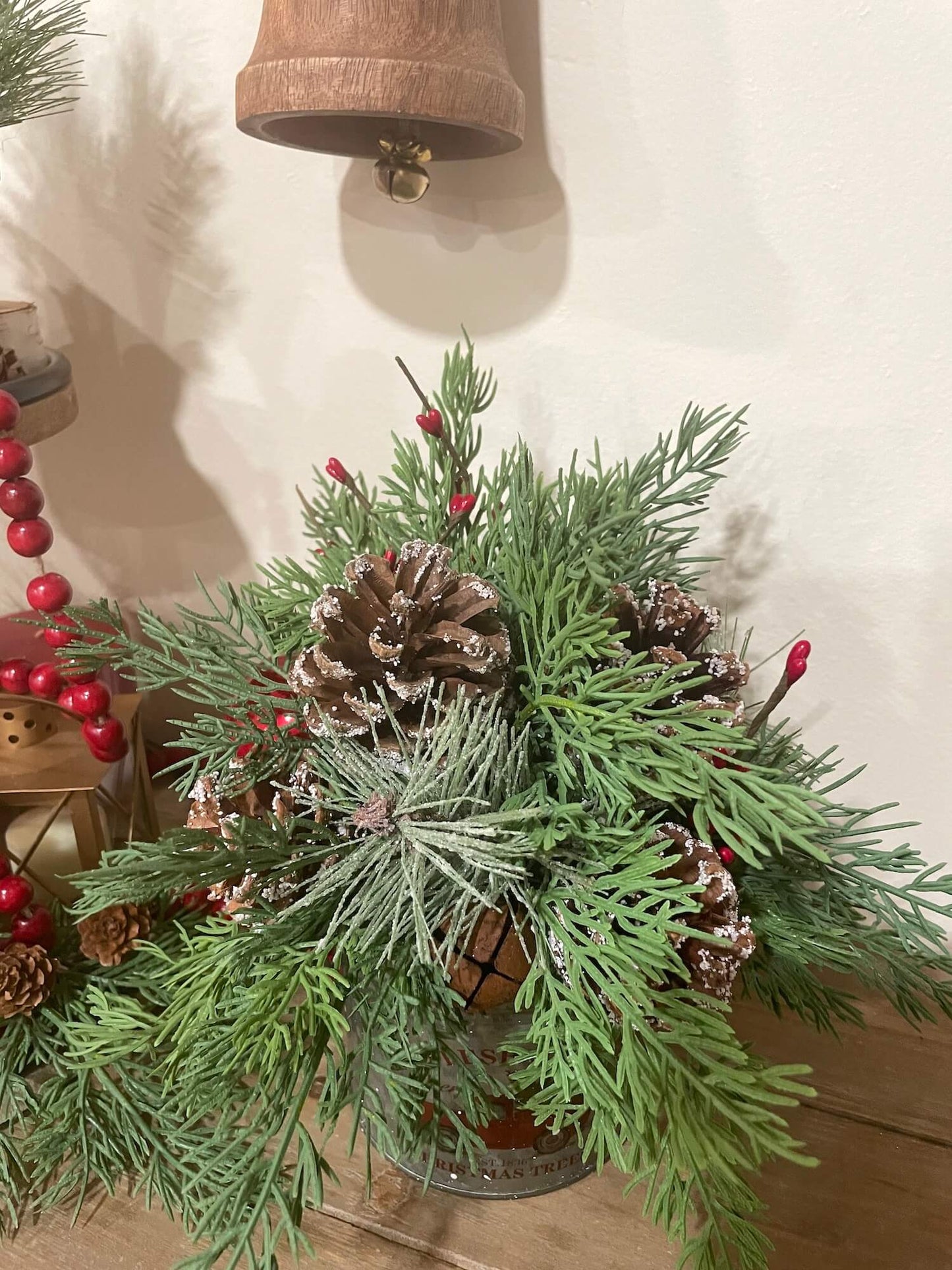 lush christmas evergreen arrangement with pinecones metal bell and red berries in metal can with red truck