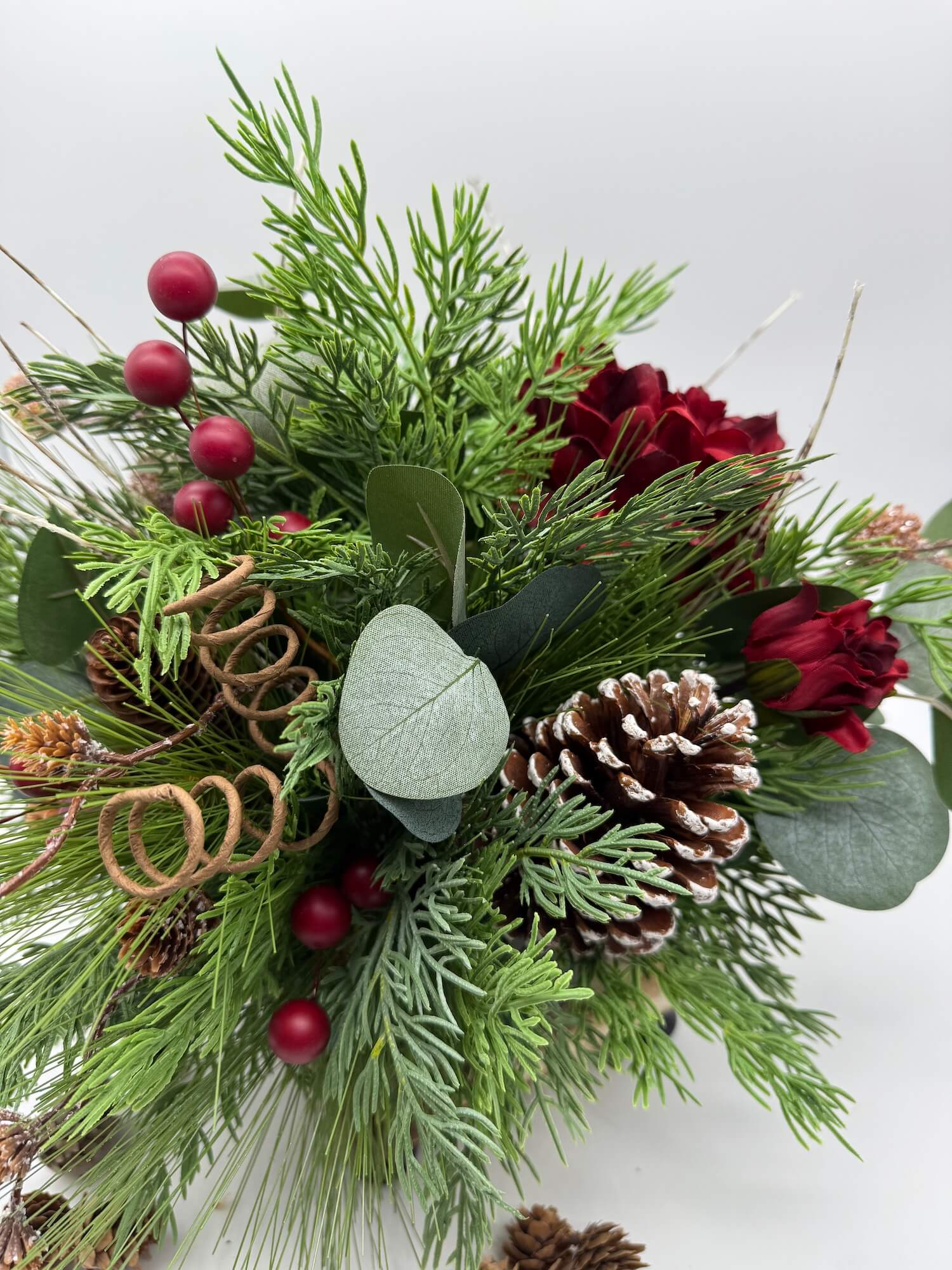high quality faux evergreen and eucalyptus stems with pinecones, red flowers and red berries in black ceramic vase