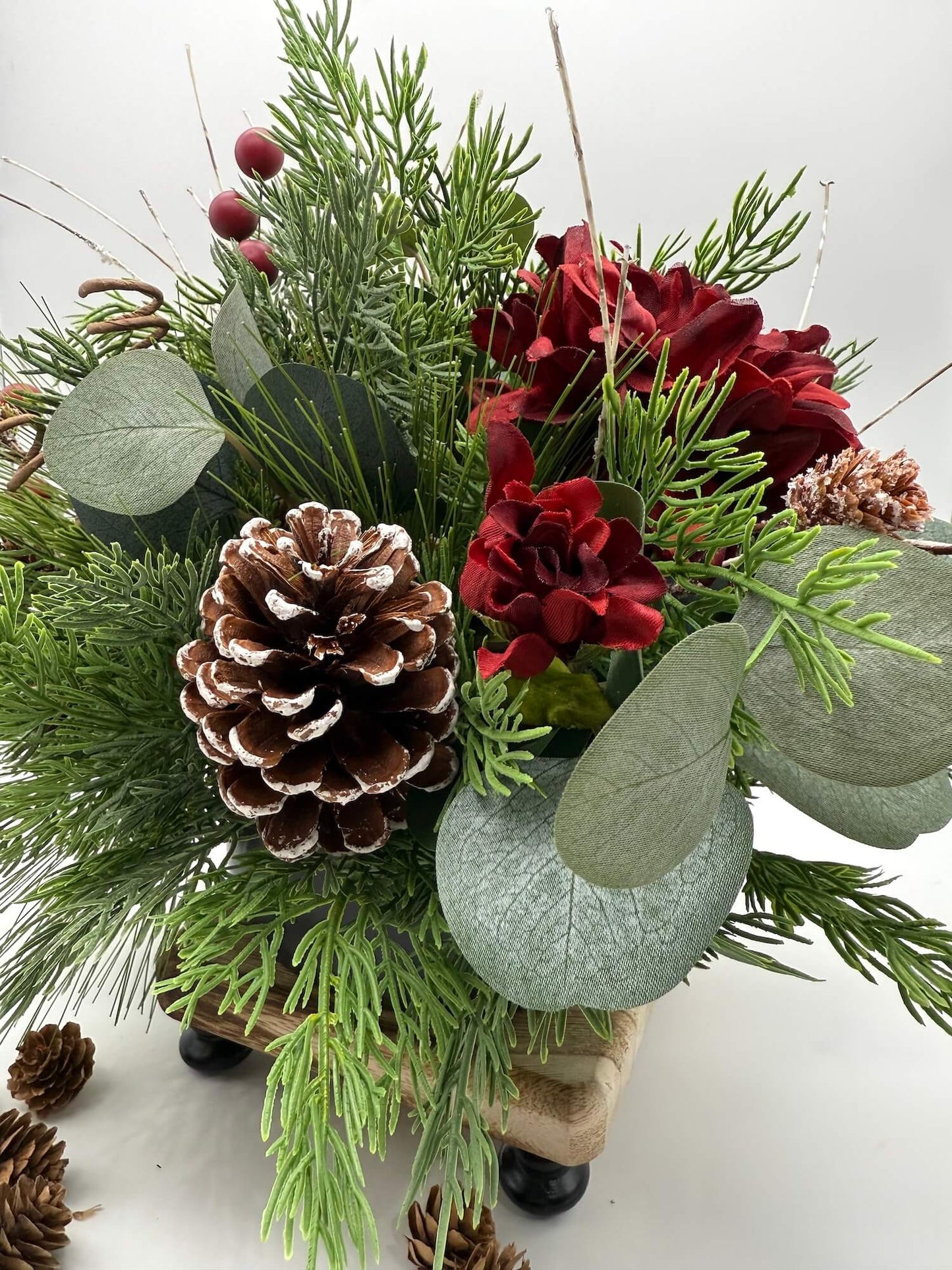 winter arrangement with evergreen and eucalyptus stems, deep red flower, red berries i neutral earthy tones in black ceramic vase