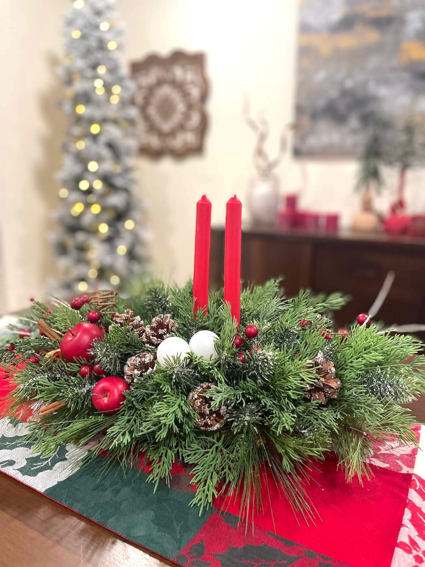 handmade elegant greenery christmas centerpiece with cinnamon stick, pinecones, red apples, slices of dried lemon and 2 red candles