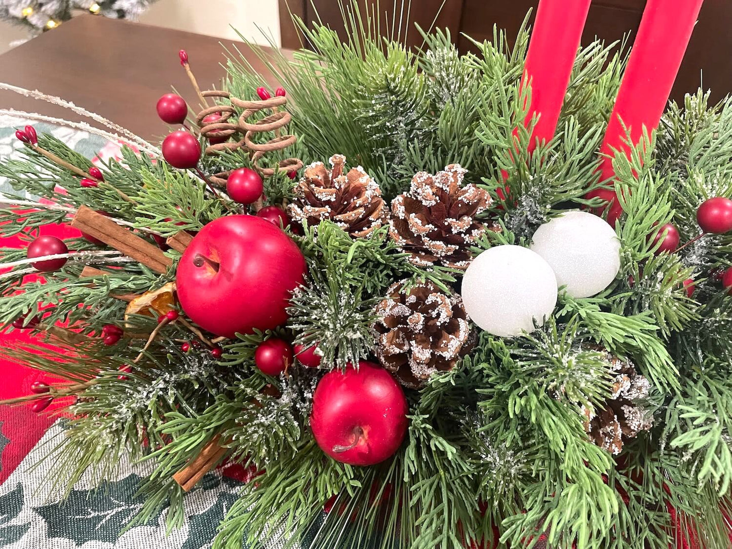 close up of front centerpiece with red apples, pinecones, cinnamon sticks, red berries and white ornaments
