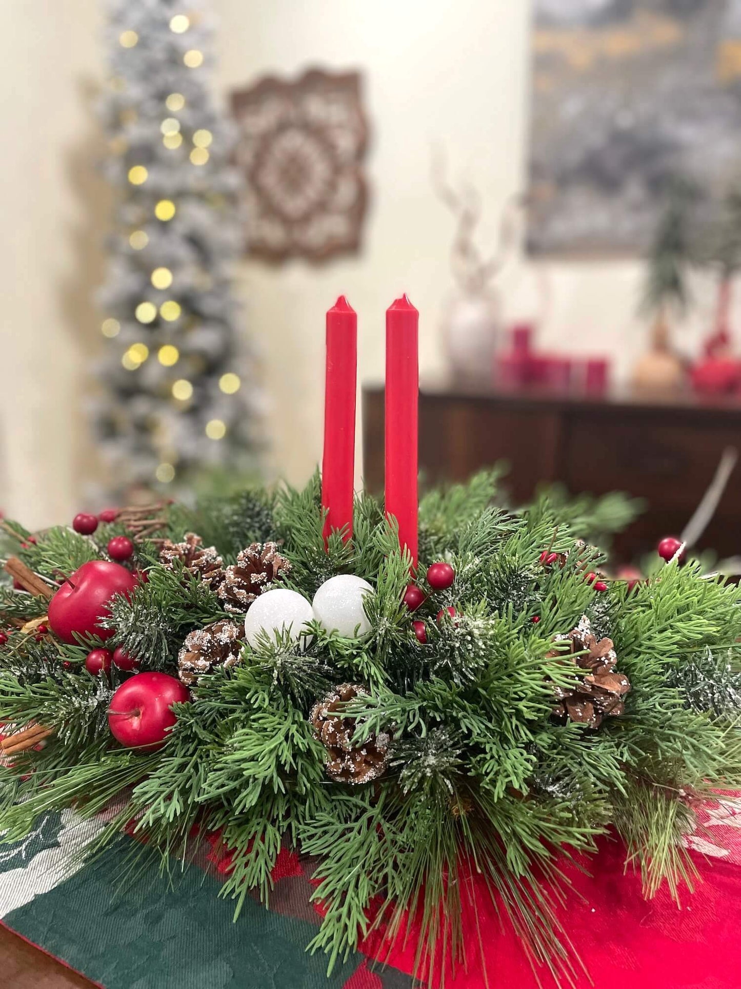 lush and realistic looking evergreen large centerpiece with pinecones, red apples, red berries, white ornaments and red tapper candles