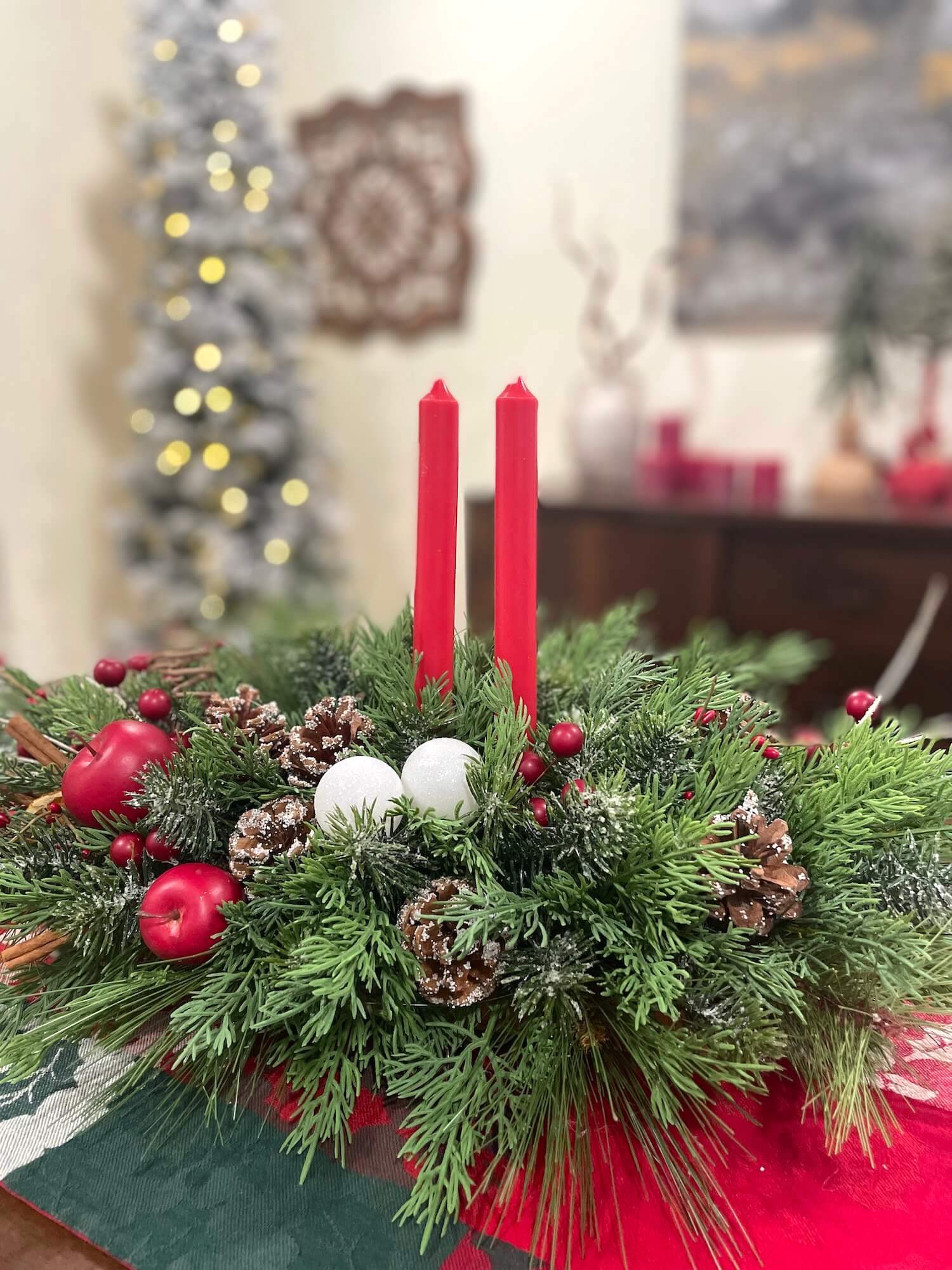 lush and realistic looking evergreen large centerpiece with pinecones, red apples, red berries, white ornaments and red tapper candles
