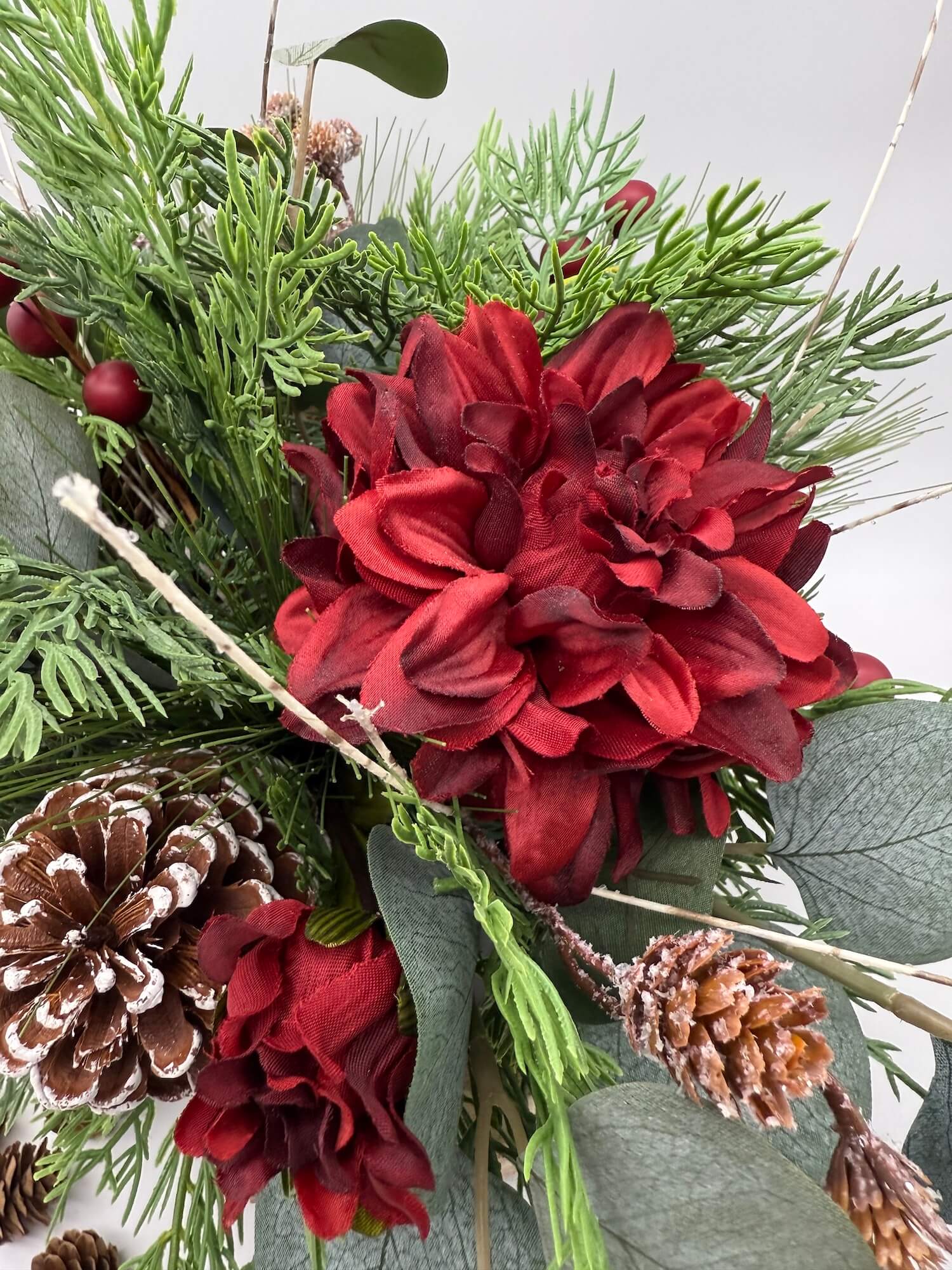 deep red flowers in winter arrangement with pinecones, variety of evergeen and eucalyptus stems