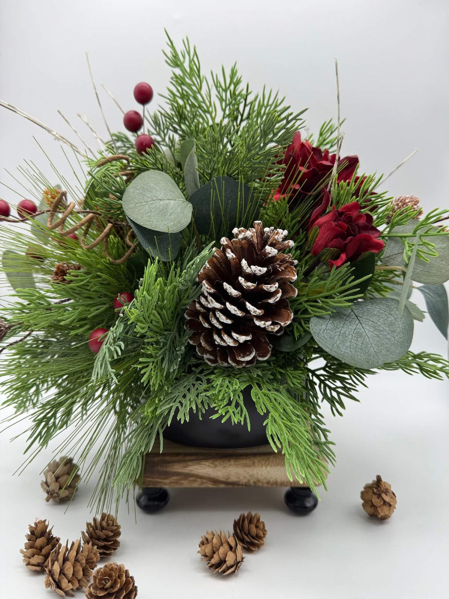 christmas centerpiece with evergreen and eucalyptus stems, red flowers, pinecones and winter berries laced in black ceramic vase