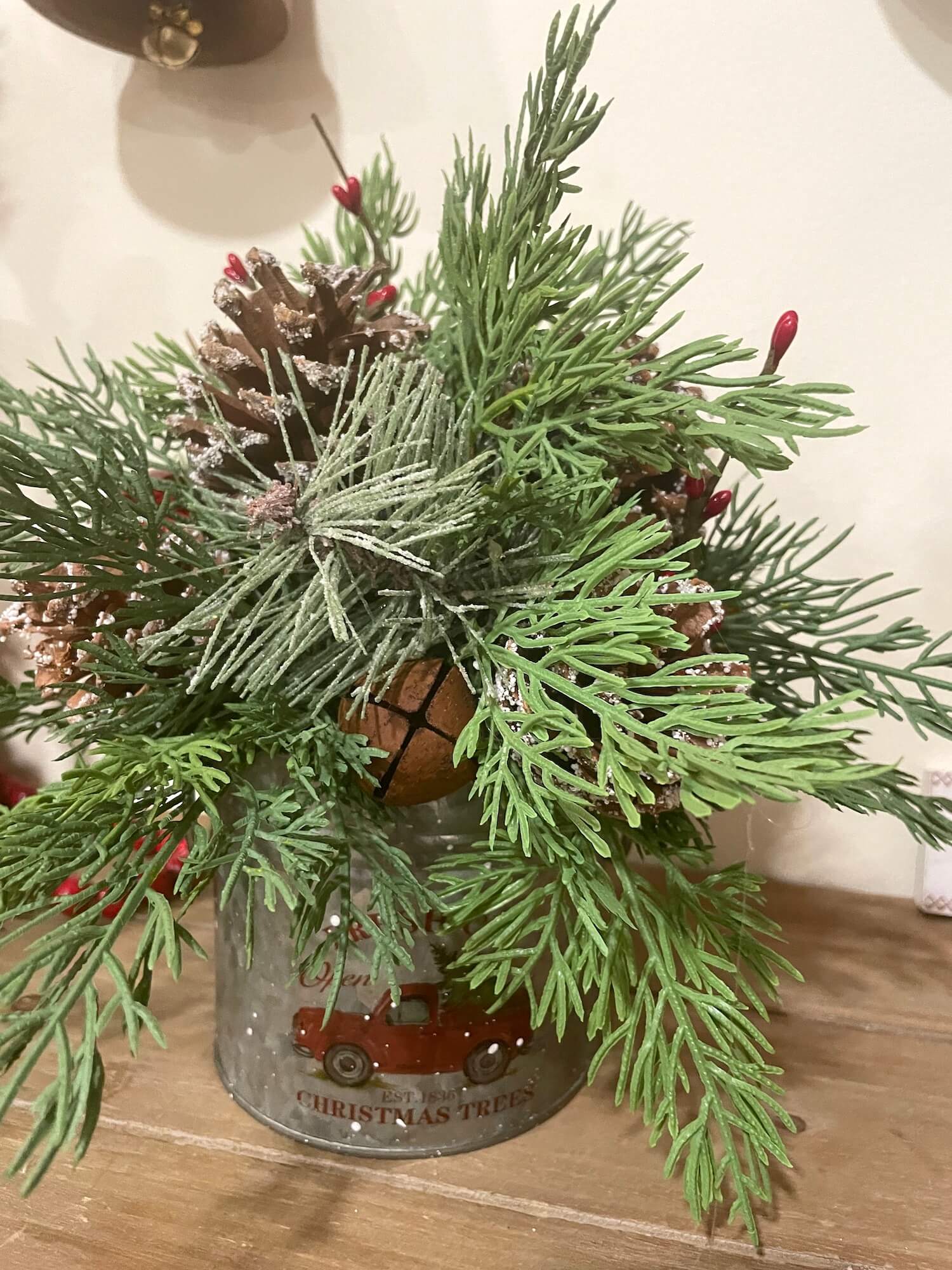 christmas arrangement with variety of evergreen, pinecones metal bell and red berries in metal can with red truck