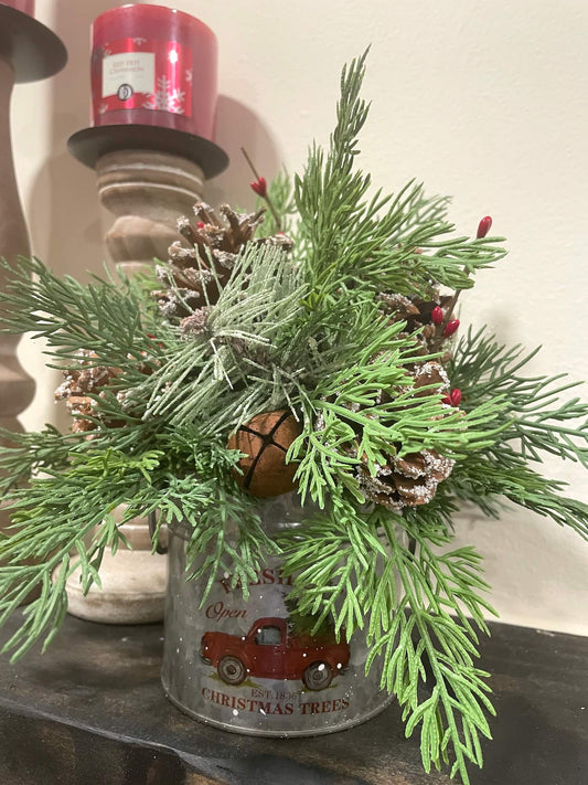 small christmas evergreen arrangement with pinecones, metal bell and red berries in metal can with red truck