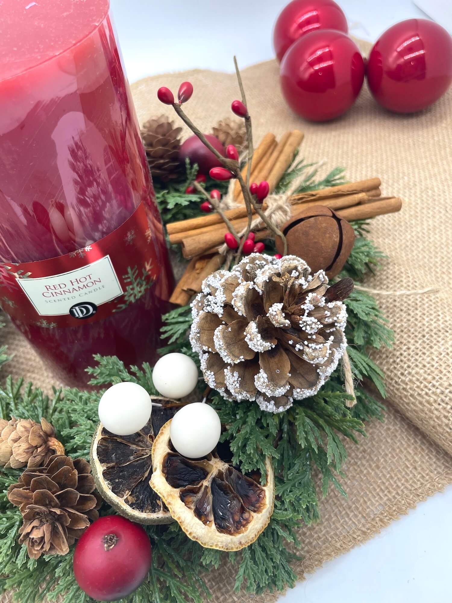 close up for Christmas evergreen table wreath arrangement with pine cones, cinnamon sticks, and red berries, metal bell