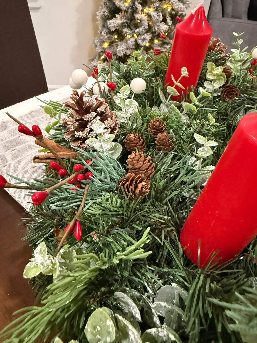 close up for lush elegant handmade advent wreath with pine, arborvitae and snowy eucalyptus stems, with snowy and plain pinecones, cinnamon sticks, red and white berries, with short thick candles or purple/pink candles set on dining table