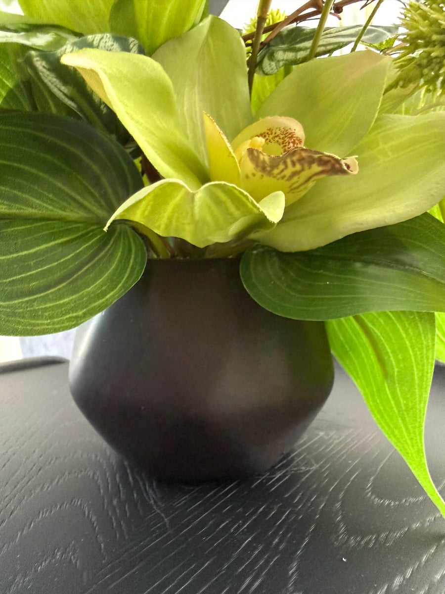 close up for vas of realistic looking green orchid small arrangement with greenery in black ceramic vase
