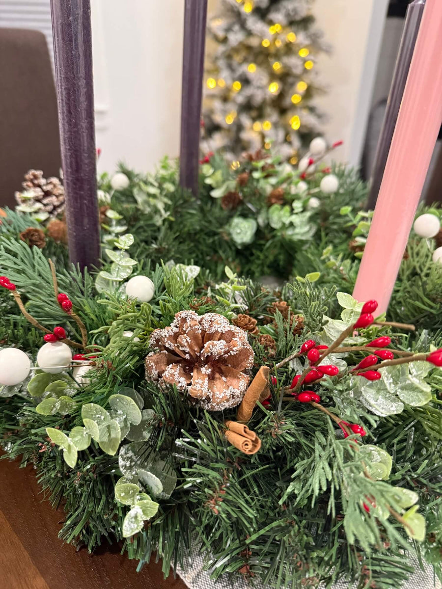 close up for handmade lush elegant evergreen advent wreath with arborvitae and snowy eucalyptus stems decorated with pinecones, red and white berries and cinnamon stick, with four taper candles in purple/pink, red or white perfect for dining table