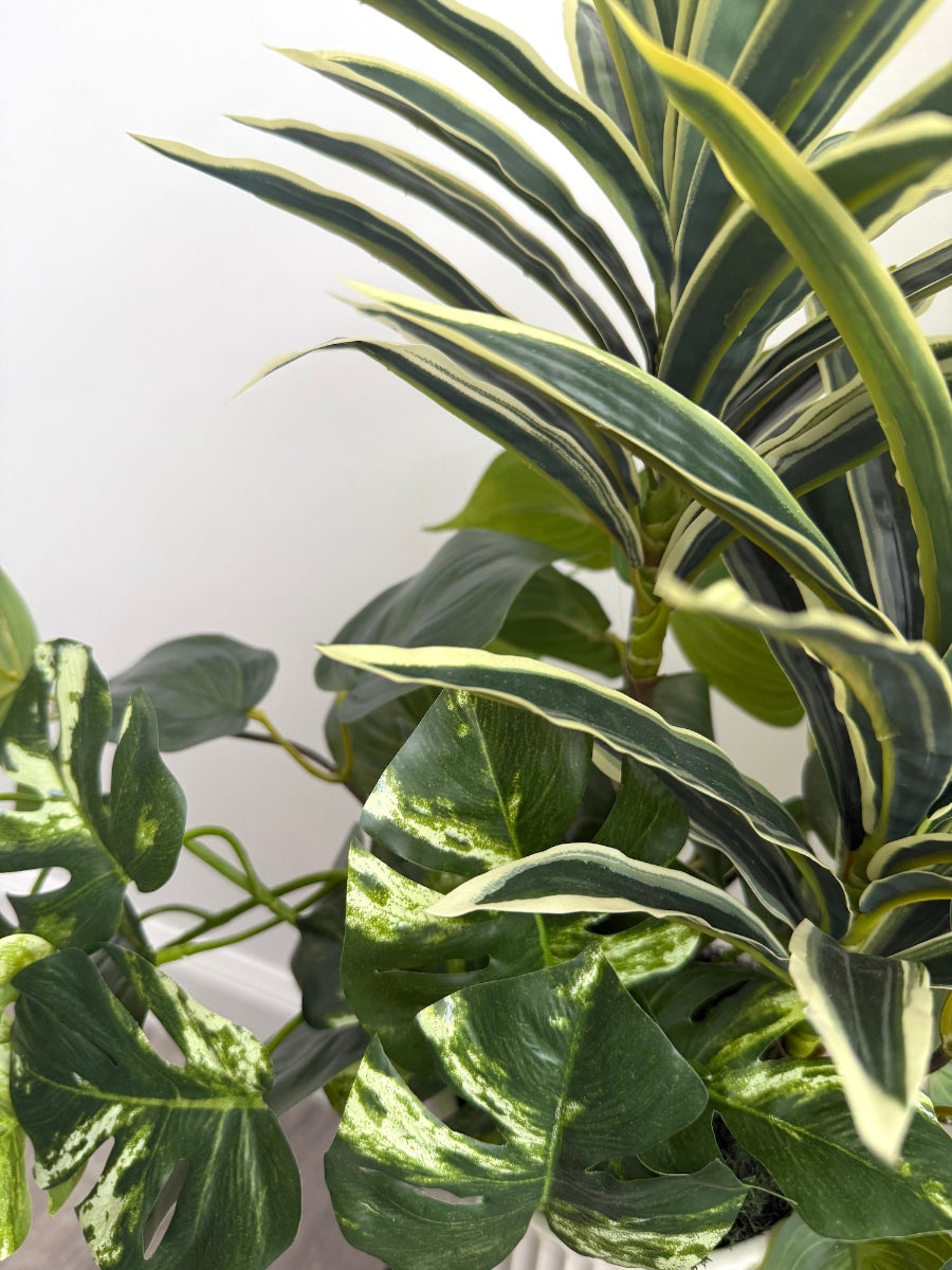 close up of tall arrangement, mix of 3 realistic looking vivid green faux plants with leaves in green and green-white, placed in tall white ceramic textured pot vase