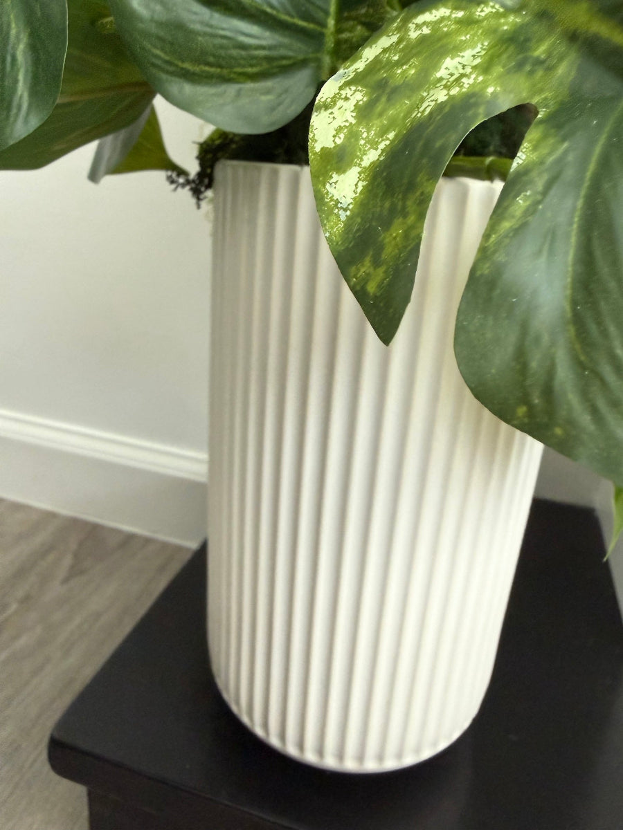 close up for pot of tall arrangement, mix of 3 realistic looking vivid green faux plants with leaves in green and green-white, placed in tall white ceramic textured pot vase
