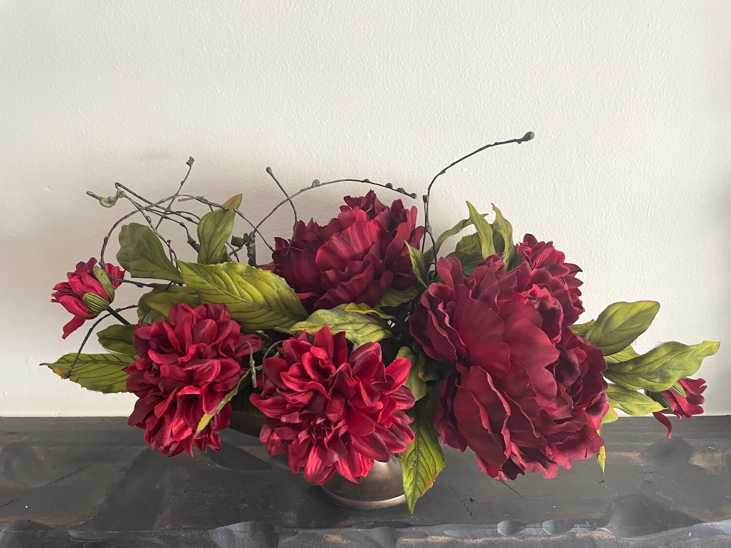 Artificial red flowers with green leaves in oval metal bronze elegant vase