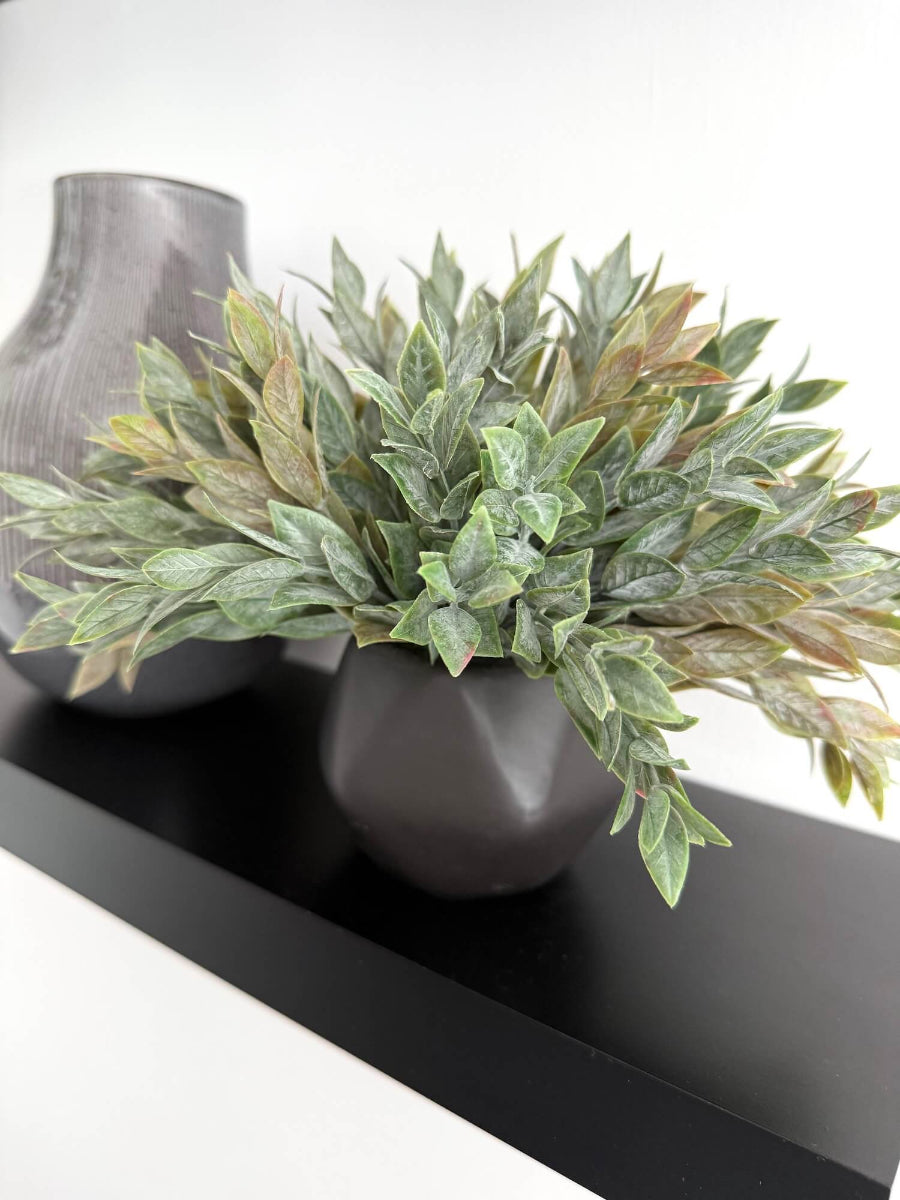 Dusty green faux plant with lush realistic foliage in a black matte geometric ceramic pot, styled for a shelf, desk, countertop, or small space