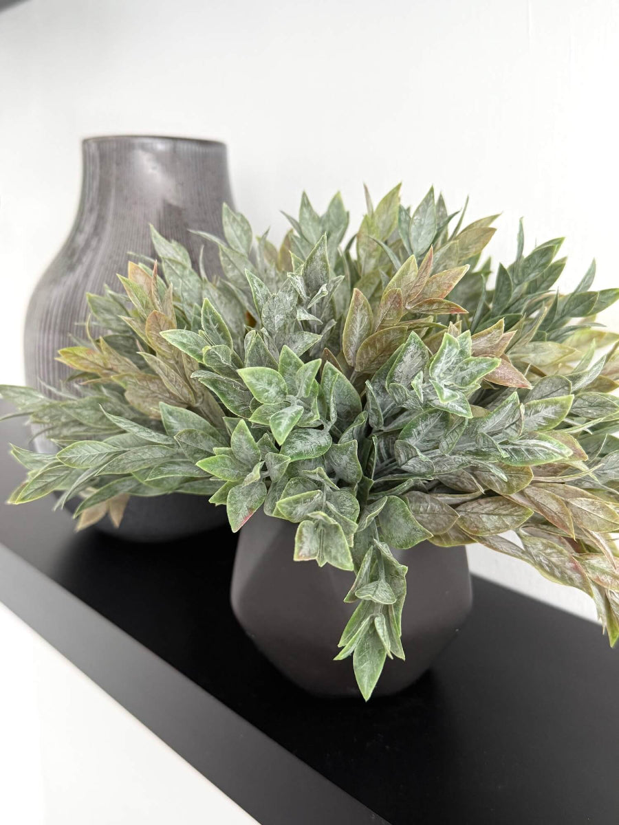 Dusty green faux plant with lush realistic foliage in a black matte geometric ceramic pot, styled for a shelf, desk, countertop, or small space