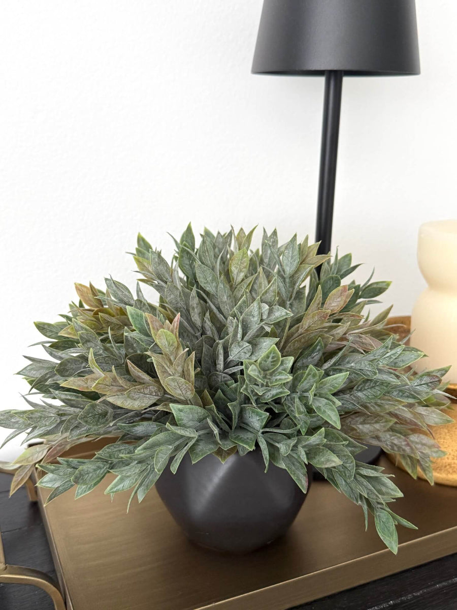 Dusty green faux plant with lush realistic foliage in a black matte geometric ceramic pot, styled for a shelf, desk, countertop, or small space