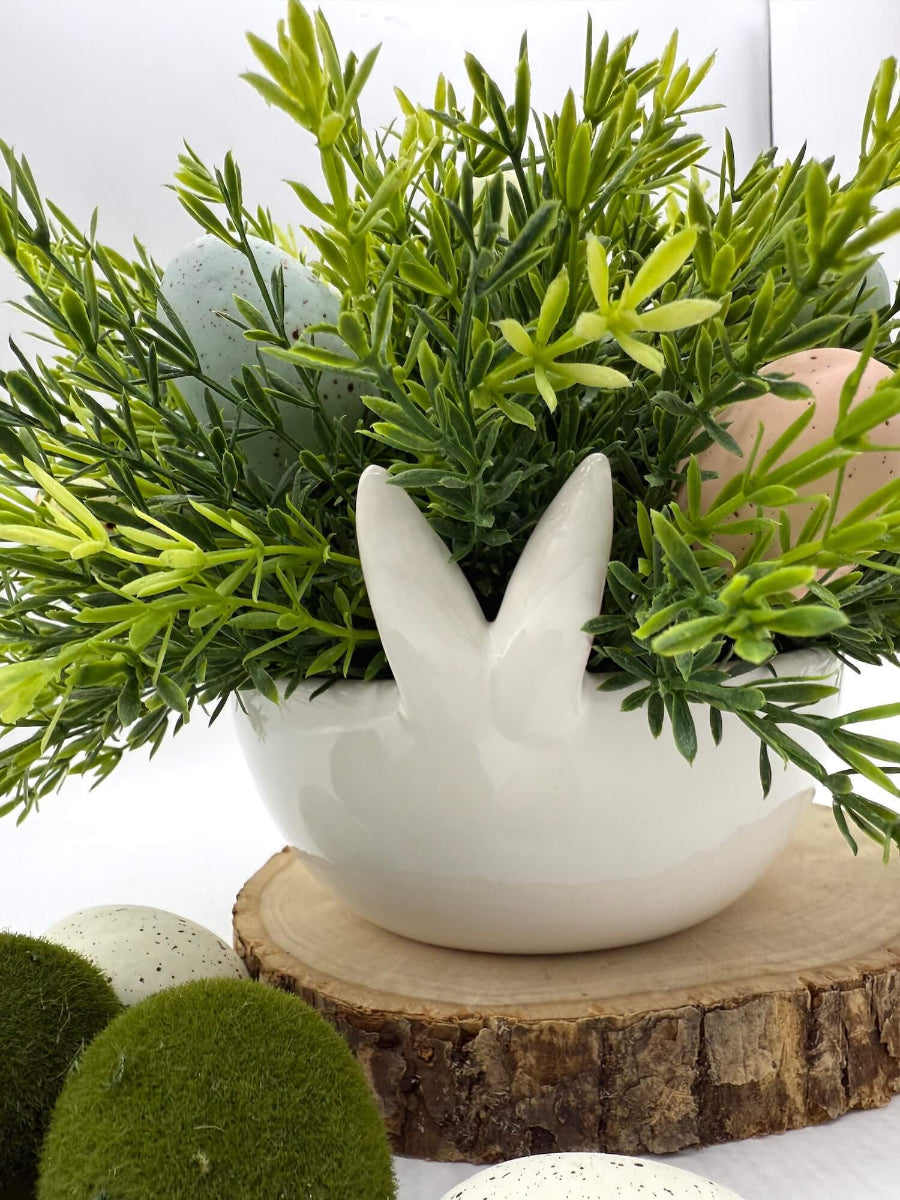 front of realistic greenery and faux eggs in white ceramic bunny bowl vase