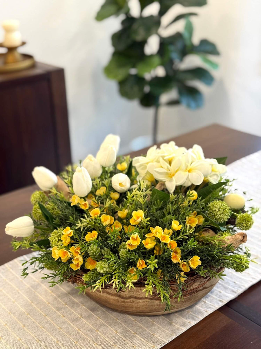 easter centerpiece with white primrose, white tulips and yellow flowers, realistic vivid greenery, driftwood display in round wooden dough bowl