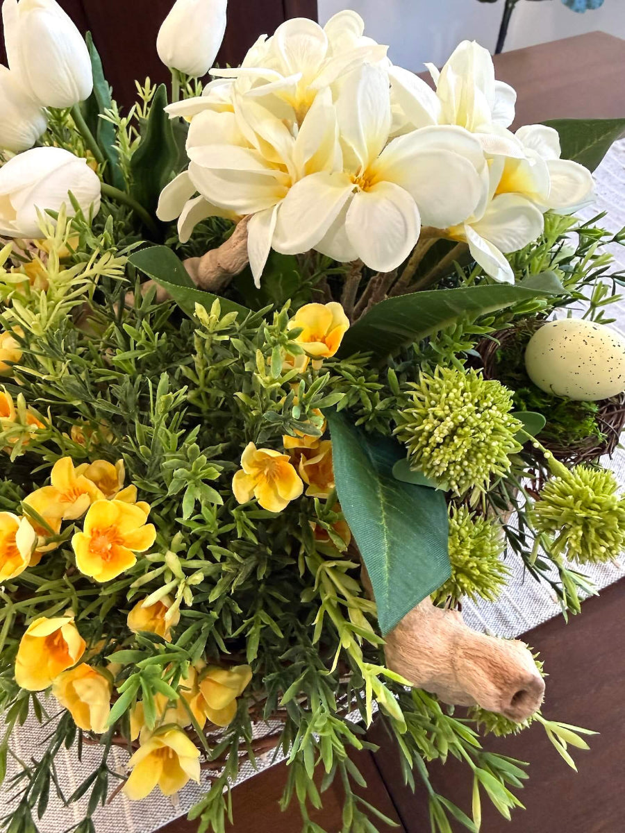 close up of easter centerpiece with white primrose, white tulips, yellow flower, realistic greenery, driftwood 