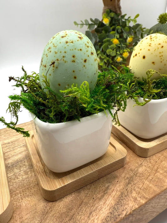 faux eggs in pastel colors in elegant shint white ceramic vases with wooden base, finished with green moss