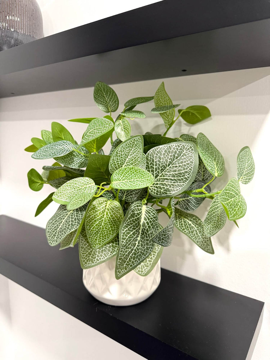 elegant realistic faux plant with green leaves with white pattern in white ceramic vase